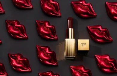 An open gold lipstick tube surrounded by a repeating pattern of metallic red sculptural lip-shaped cases on a dark background.