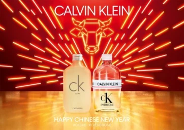 Two Calvin Klein perfume bottles standing on a reflective golden surface against a red neon bull graphic background