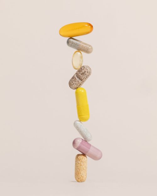 Stack of colourful vitamin capsules against a plain background. Pills in yellow, grey, beige, yellow, white, and pink colors.