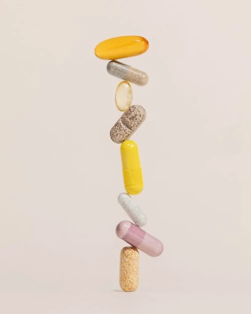 Stack of colourful vitamin capsules against a plain background. Pills in yellow, grey, beige, yellow, white, and pink colors.