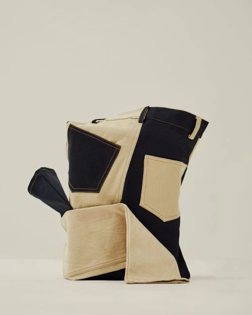 Close-up studio shot of a geometrically folded sculptural pair of bi-color denim pants in a neutral studio setting with soft lighting.