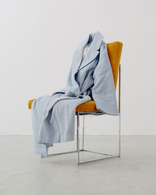 Light blue plaid coat draped over a yellow and silver metal chair in a white room. Minimalist fashion still life.