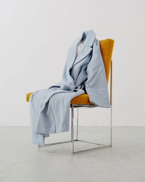 Light blue plaid coat draped over a yellow and silver metal chair in a white room. Minimalist fashion still life.