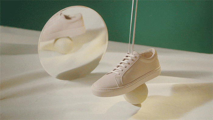Beige sneaker shoe in studio product shot with a mirror and a background of green and beige colors, with the sneaker floating on a sphere.