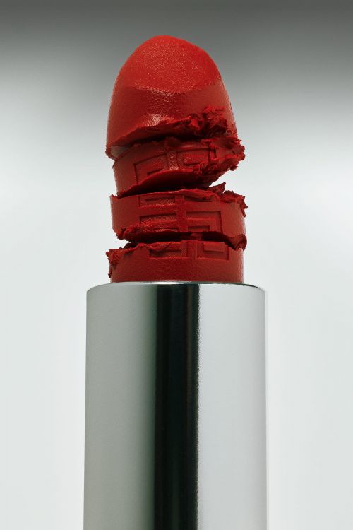 Macro studio shot of a bright red lipstick with a silver tube against a neutral gradient background, showcasing beauty product.