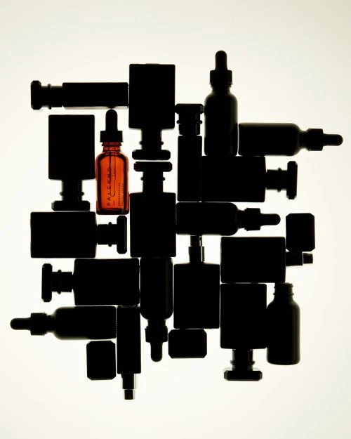 Still life shot of assorted amber and black glass bottles in a grid-like arrangement, contrasting colors against a white backdrop.