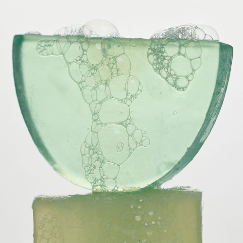 Close-up of a translucent green soap bar with bubbles on top, set against a plain white background, highlighting its texture.