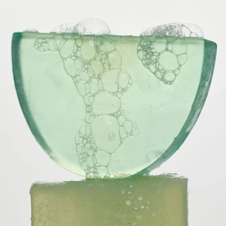 Close-up of a translucent green soap bar with bubbles on top, set against a plain white background, highlighting its texture.