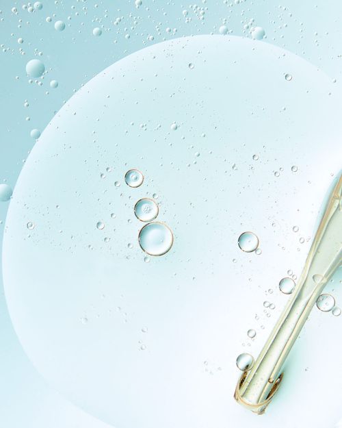 Close-up of clear serum with suspended oil droplets on light blue, creating a fresh and hydrating appearance suitable for beauty product.