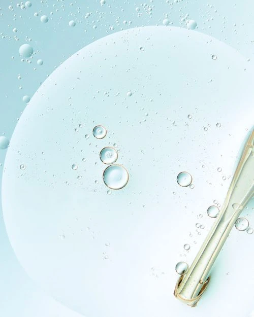 Close-up of clear serum with suspended oil droplets on light blue, creating a fresh and hydrating appearance suitable for beauty product.