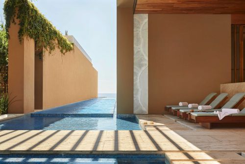 Outdoor luxury spa area with a swimming pool, tiled deck, and sunbeds, showcasing a peaceful and high-end wellness environment.