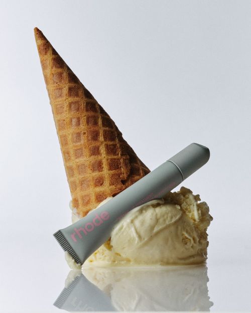 Cosmetic tube rests on melting vanilla ice cream with waffle cone against a white background in a studio shot.
