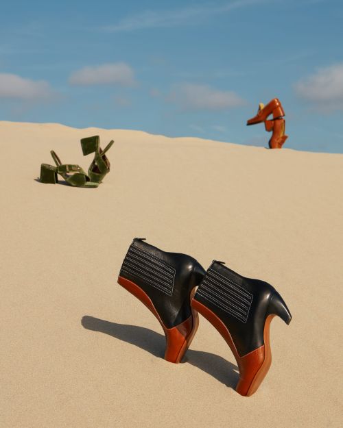 Fashion-forward footwear showcased in a surreal desert setting, featuring high-heeled boots and platform sandals against a clear blue sky.