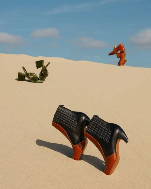 Fashion-forward footwear showcased in a surreal desert setting, featuring high-heeled boots and platform sandals against a clear blue sky.