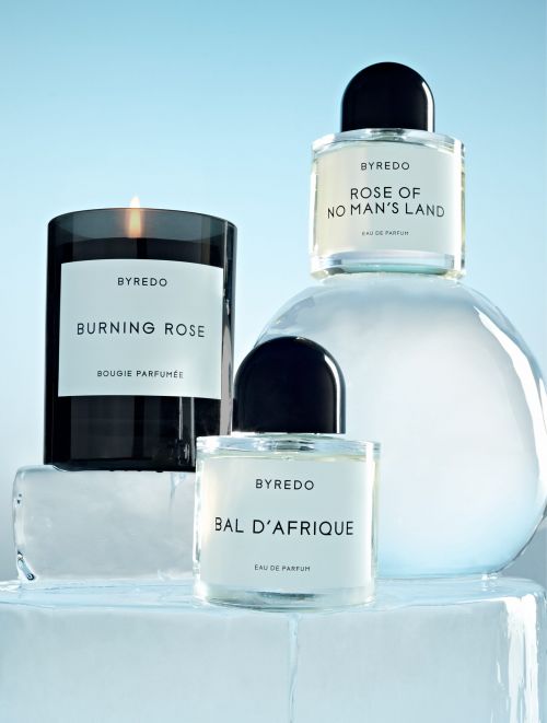 Still life of Byredo candle and perfume bottles on an ice block against a light blue background, showcasing the brand's fragrance line.