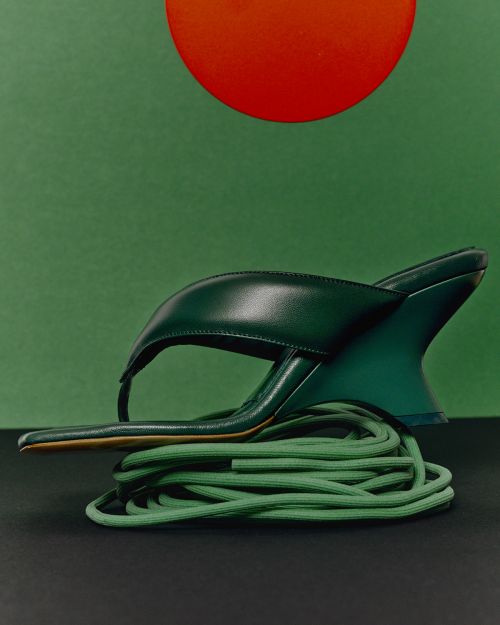 Elevated studio shot of a single green sandal with a geometric heel perched atop bundled green cord against a two-tone green backdrop.