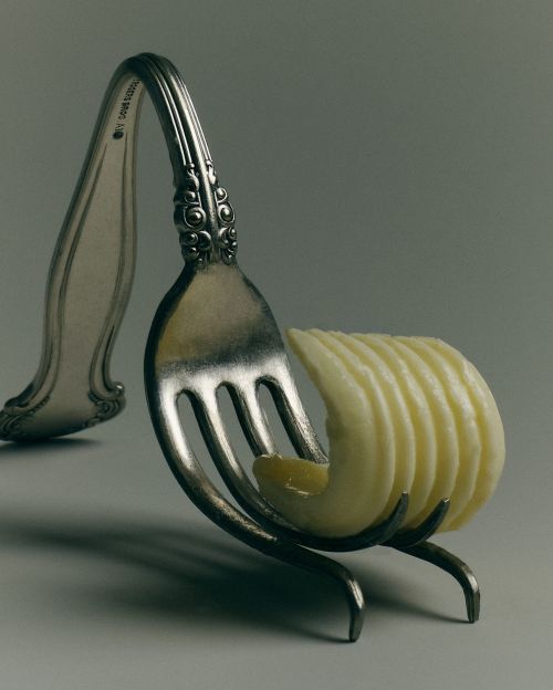 Close-up studio shot of a pat of butter on the tines of a silver fork, set against a neutral grey backdrop with shadows.