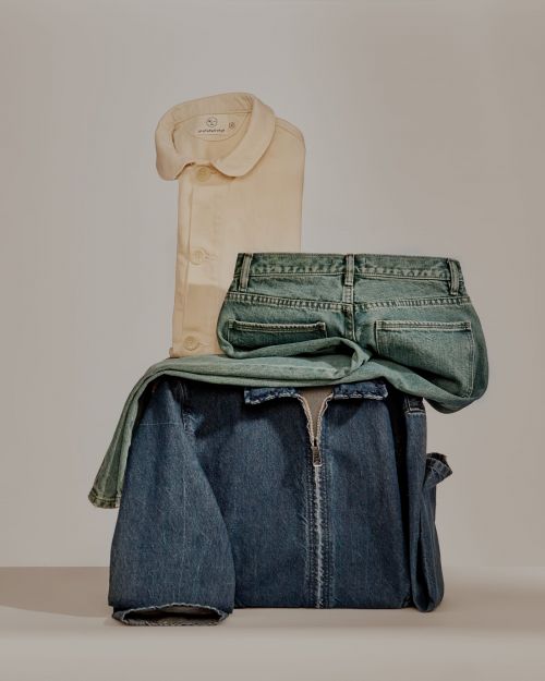 Fashion still life featuring folded denim jacket, cream-colored button-down shirt, and acid wash jeans against a neutral backdrop.