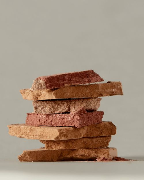 Stacked powder eyeshadow samples in neutral tones, ranging from light beige to deep terracotta, displayed against a solid grey background.