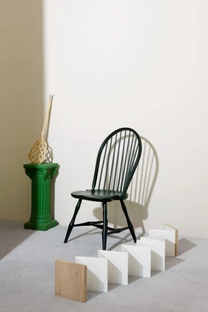 Interior design scene featuring a black spindle chair on a grey carpet, with a green column pedestal and decorative straw object.