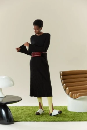 Elegant Black Woman in Ribbed Midi Dress with Burgundy Belt Bag Stands on Green Rug in Fashion Editorial Photo.