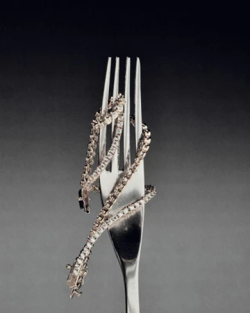 Diamond tennis bracelet coiled around a silver fork against a grey gradient backdrop, emphasizing luxury and culinary fusion in jewelry.