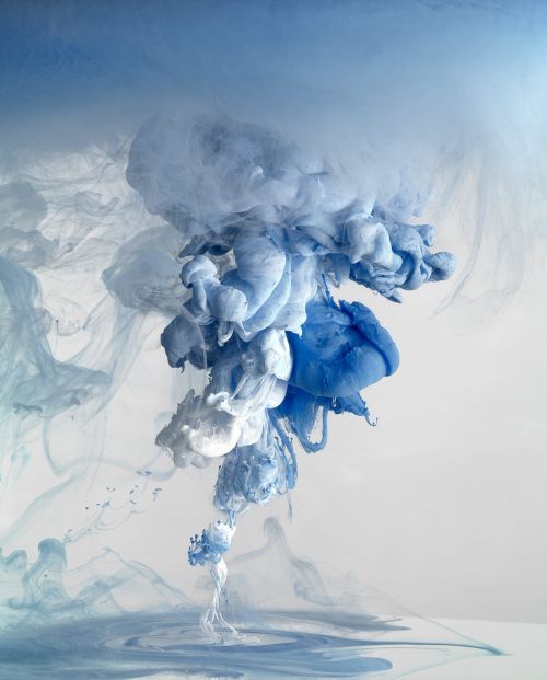 Artistic visual of flowing blue and white inks mixing in water, creating soft and dreamy abstract shapes against a neutral background.