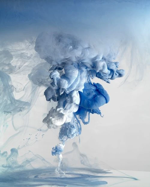 Artistic visual of flowing blue and white inks mixing in water, creating soft and dreamy abstract shapes against a neutral background.