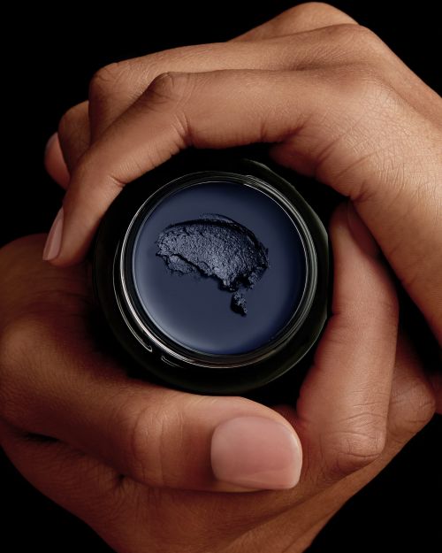 Close-up shot of hands holding a jar of dark blue cream against a black background, showcasing skincare or cosmetic product.