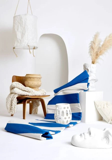Indoor studio shot featuring a wooden chair with a draped blanket, a striped blue and white textile, decorative vases, and a hanging lamp.