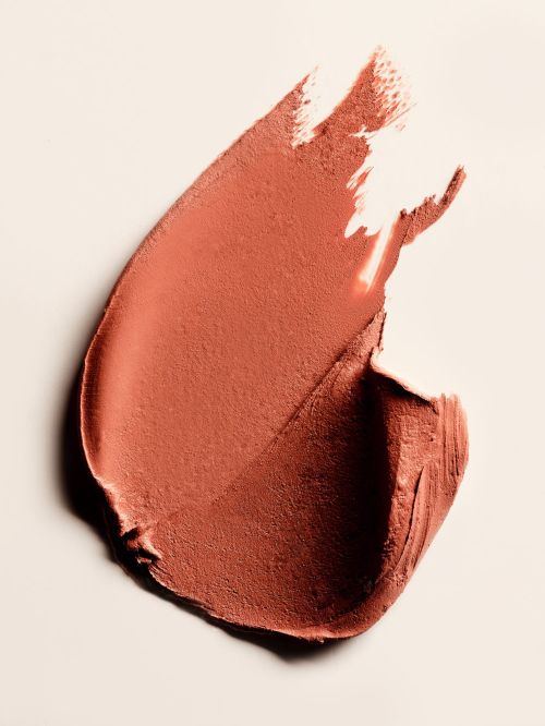 Close-up of a smear of terracotta-colored lipstick against a pale, neutral background. Beauty, cosmetic, and makeup concept.