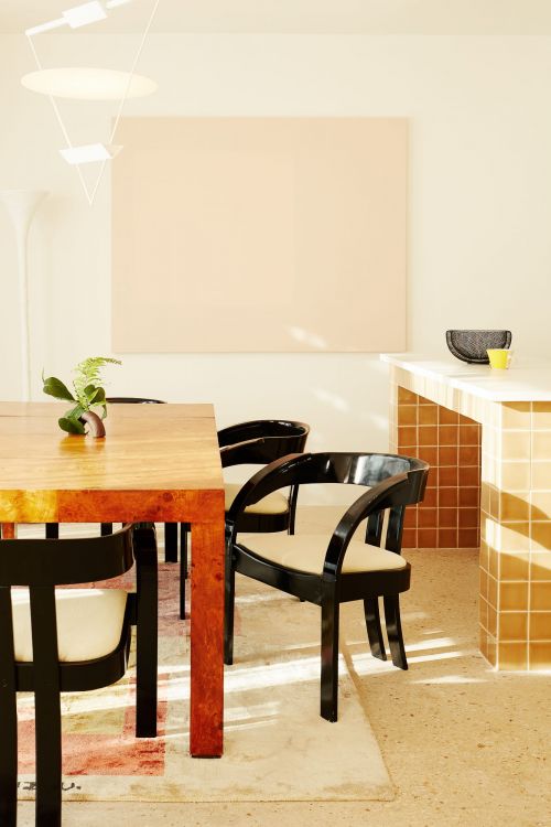 Dining room interior with a wooden table set, black chairs, and light neutral color scheme. A modern overhead light fixture hangs above.