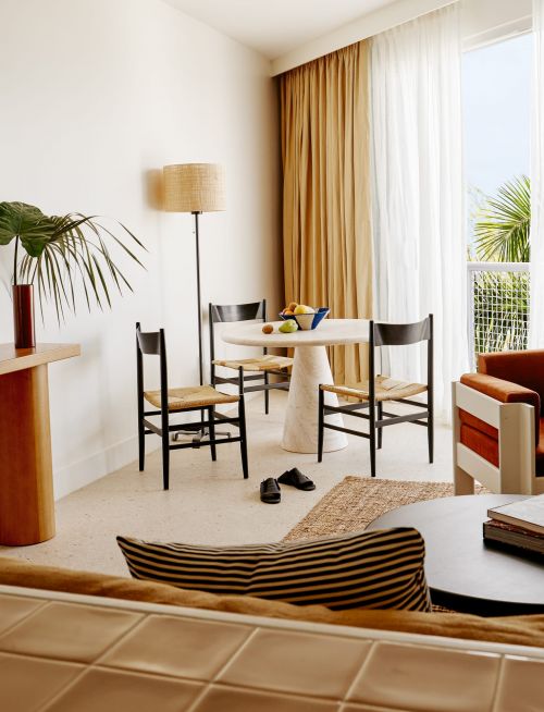Interior of a minimalist room featuring a round dining table, chairs, a floor lamp, a plant, and modern decor, with a bright, airy ambiance.