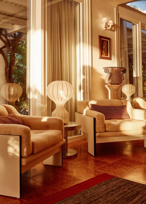 Cozy living room interior with two modern armchairs, stylish lamps, artwork, neutral color palette, and large windows with natural light.