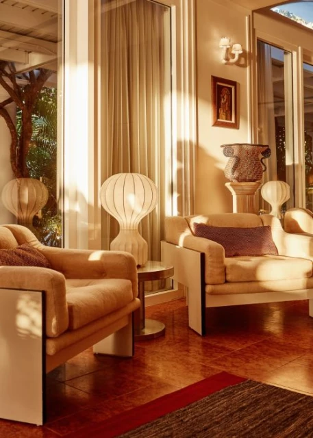 Living room interior with two beige armchairs, a small round side table, and decorative lamps, bathed in warm, inviting sunlight.