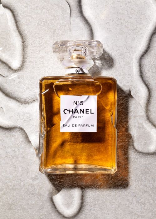 A product shot captures a glass Chanel No. 5 perfume bottle with golden liquid on a textured gray background, featuring visible product branding.
