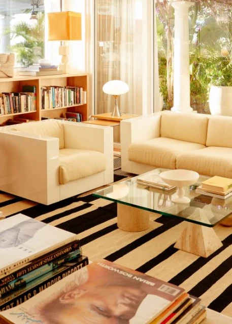 Living room interior featuring a cream sofa and chair, glass coffee table, bookshelf, and black and white striped rug creating a modern aesthetic.
