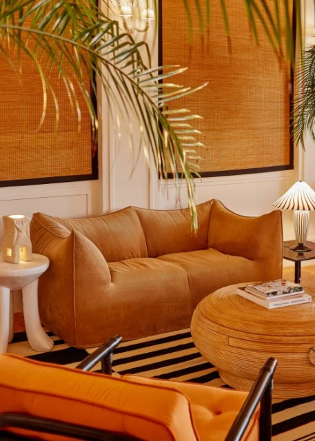 Living room interior featuring a caramel brown couch, patterned rug, round table, and palm fronds, creating a warm, inviting atmosphere.