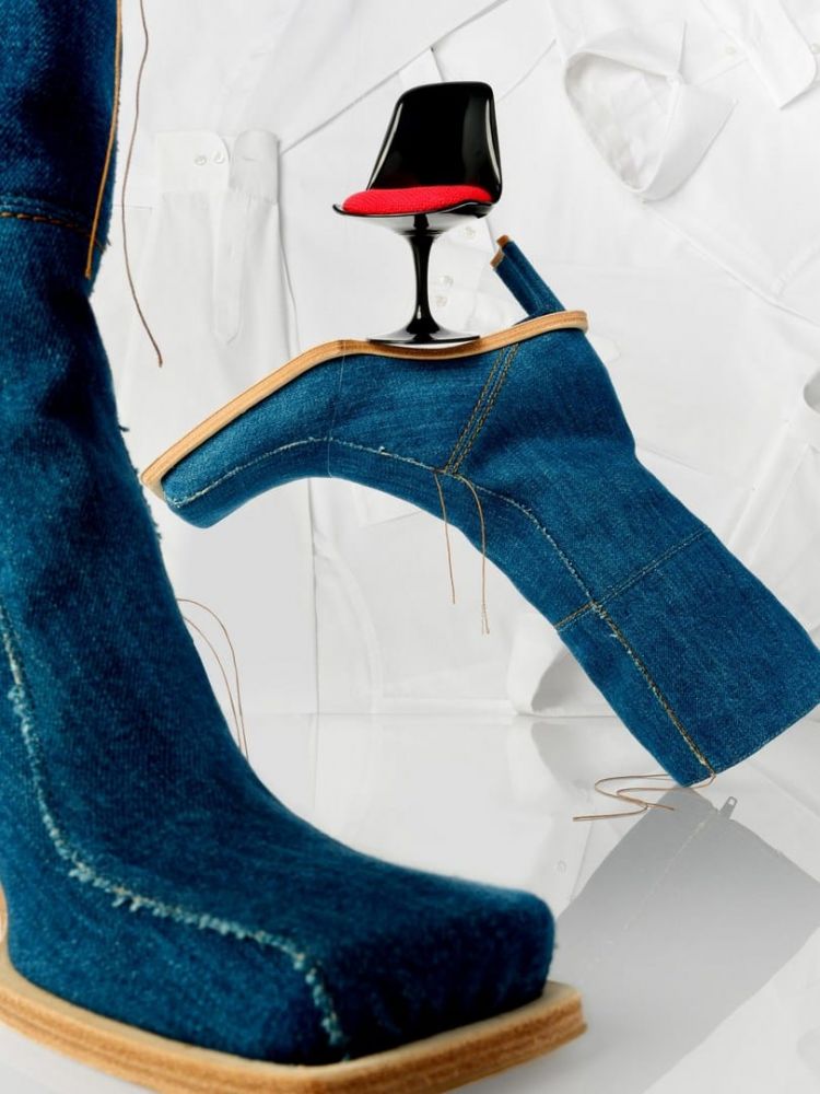 Surreal fashion still life with a denim boot, miniature chair, and white button-down shirts creating an artful, visually arresting composition.