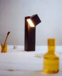 Modern black geometric table lamp with an illuminated angled cube head on a white tabletop with amber glassware