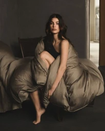 Woman wrapped in a taupe blanket sitting on a bed in a moody room styled by Jessie Cundiff