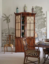 Antique wooden corner cabinet in a dining room with animal print upholstered chairs and hand-painted scenic wallpaper
