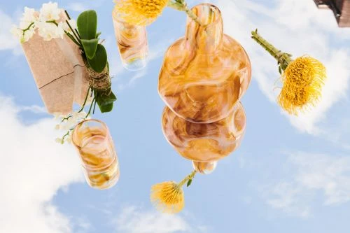 Glass vases and floral arrangements displayed against a bright sky backdrop, creating a dreamy and artistic still life composition.