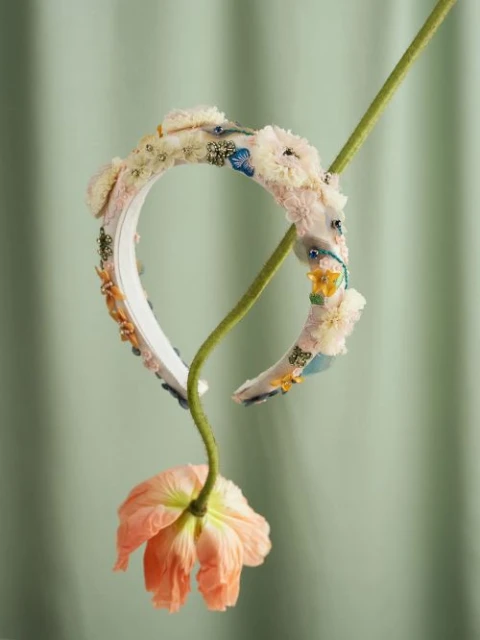 Floral headband accessory featuring off-white and peach flowers and green stem on a pastel green background for a nature-themed aesthetic.