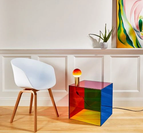 Interior design featuring a modern white chair with wooden legs next to a colorful acrylic cube table with a round orange lamp.