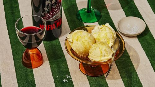 A photo showcasing a wine bottle and glass beside ice cream in a bowl, set on a green and white striped tablecloth, creating an inviting still life.