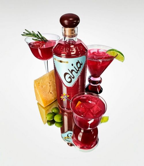 Close-up of a bottle of Ghia non-alcoholic aperitif surrounded by cocktails, garnished with rosemary and lime, and a chunk of cheese.