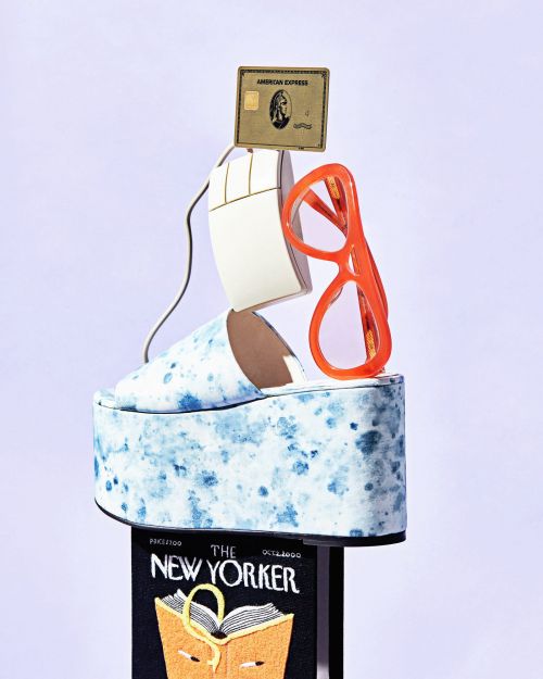 Whimsical composition featuring a platform shoe, computer mouse, eyeglasses, credit card, and magazine on a white gradient background.
