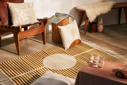 Interior still life of a rug with geometric design, wood furniture, throw pillows, drinkware, tangerines, and decor elements.