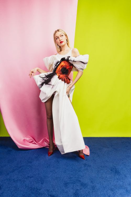 Fashion photo of a woman in an avant-garde white dress posing in front of a pink and green backdrop with a blue carpet.